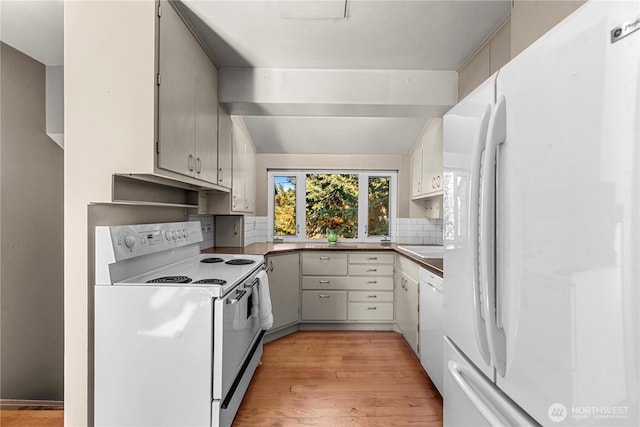 kitchen with lofted ceiling, white appliances, backsplash, and light wood finished floors