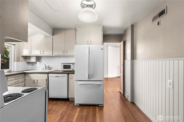 kitchen featuring visible vents, light wood-style flooring, white cabinets, a sink, and white appliances