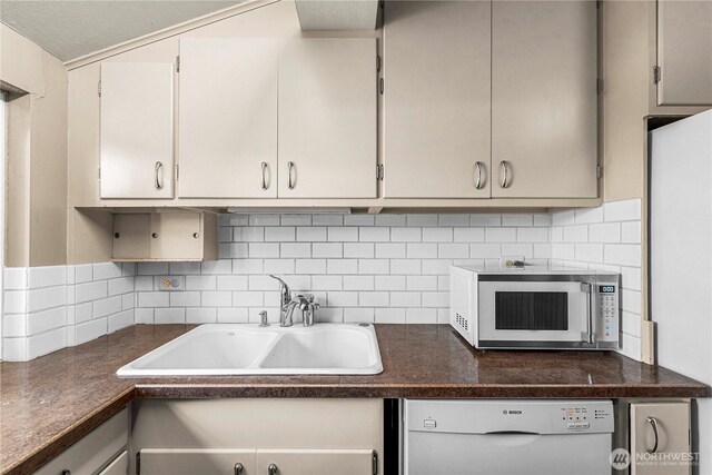 kitchen featuring tasteful backsplash, dishwasher, dark countertops, freestanding refrigerator, and a sink