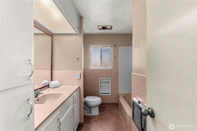 bathroom featuring tile walls, toilet, heating unit, vanity, and a bath