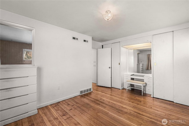 unfurnished bedroom featuring hardwood / wood-style floors, visible vents, and baseboards