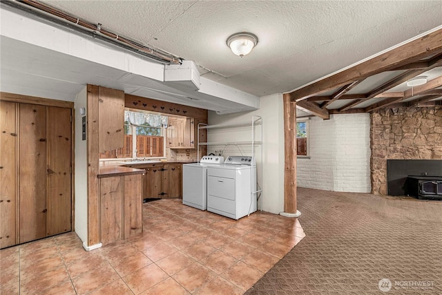 laundry area with washer and clothes dryer, a wood stove, light carpet, brick wall, and laundry area