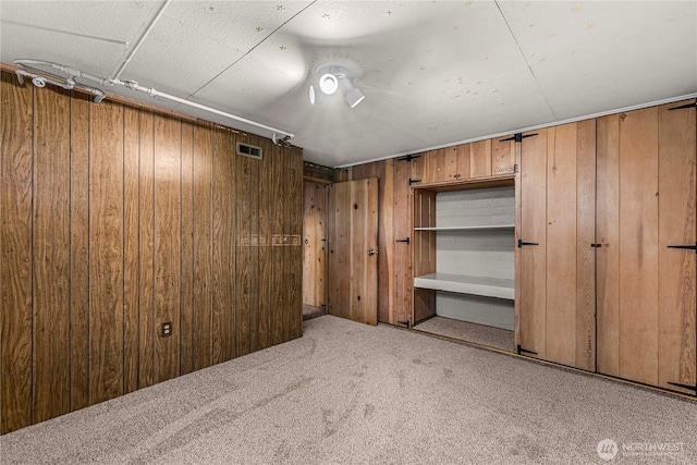 carpeted empty room featuring wood walls and visible vents