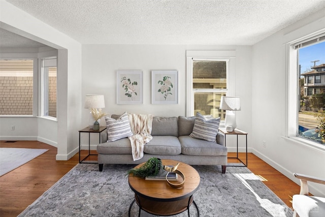 living room featuring a textured ceiling, baseboards, and wood finished floors