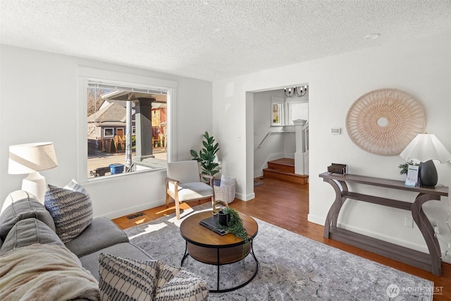 living area with a textured ceiling, stairway, baseboards, and wood finished floors