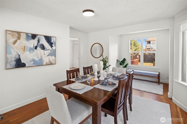 dining room with a textured ceiling, baseboards, and wood finished floors