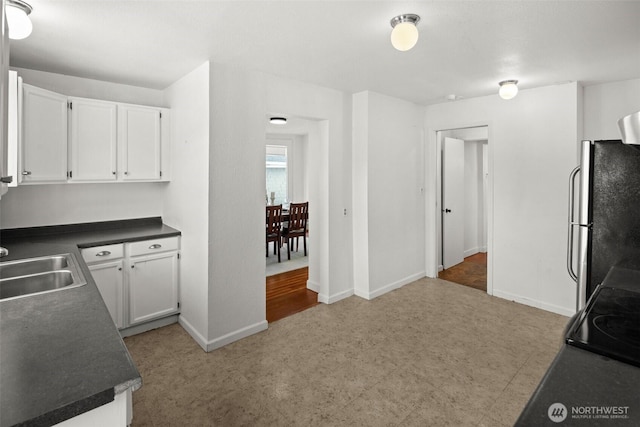 kitchen with baseboards, dark countertops, freestanding refrigerator, and white cabinetry