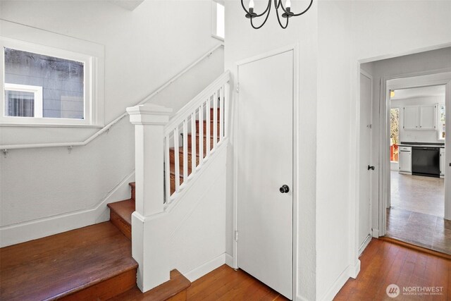 staircase featuring wood-type flooring, a notable chandelier, and baseboards