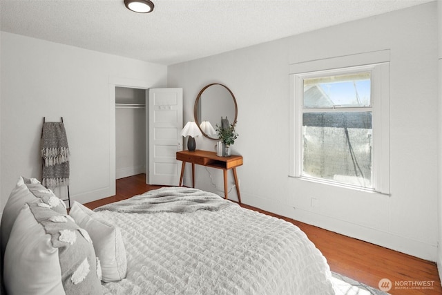 bedroom with a textured ceiling, a closet, wood finished floors, and baseboards