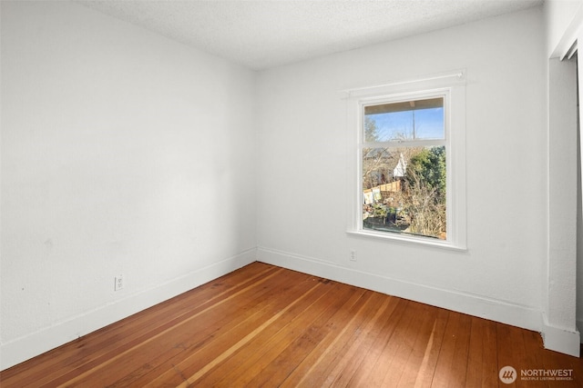 empty room featuring a textured ceiling, hardwood / wood-style floors, and baseboards