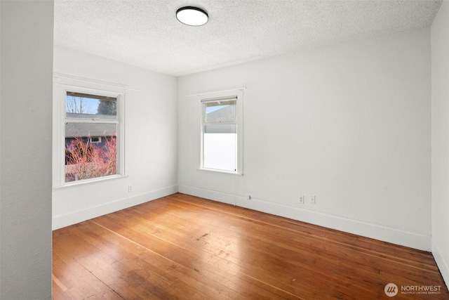 spare room with light wood-style floors, a textured ceiling, and baseboards