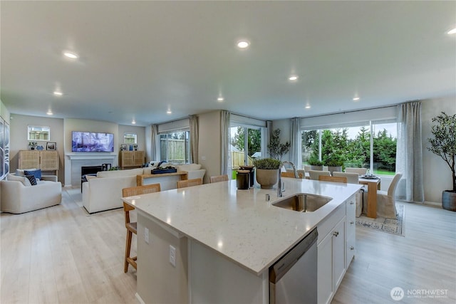 kitchen with a fireplace, stainless steel dishwasher, open floor plan, white cabinets, and a sink