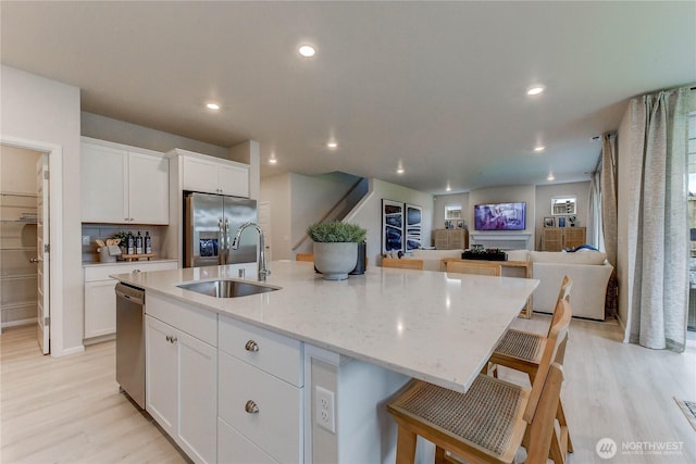 kitchen with a kitchen island with sink, a sink, white cabinets, open floor plan, and appliances with stainless steel finishes