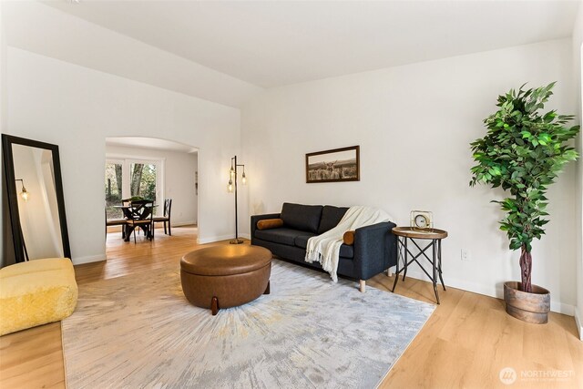 living room featuring arched walkways, vaulted ceiling, baseboards, and wood finished floors