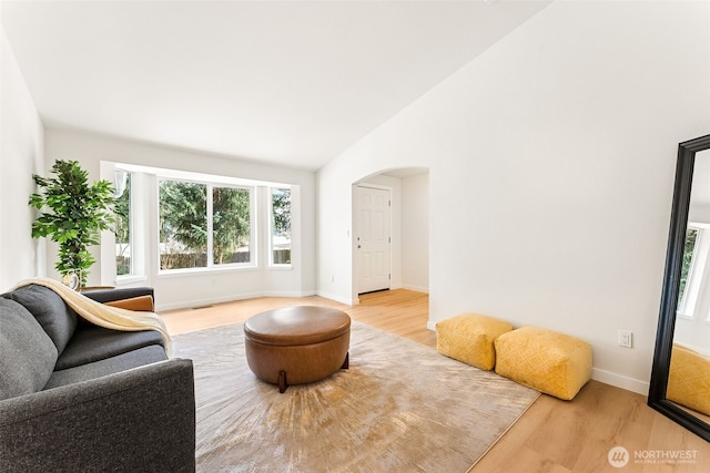 living area with visible vents, baseboards, lofted ceiling, light wood-style floors, and arched walkways