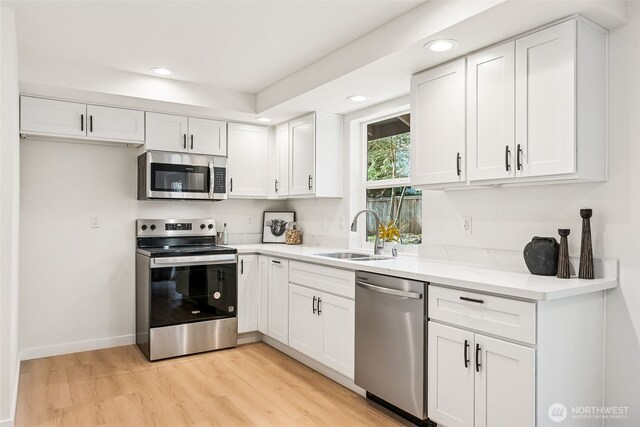 kitchen with light wood finished floors, light countertops, white cabinets, stainless steel appliances, and a sink