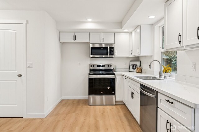 kitchen featuring a sink, stainless steel appliances, light wood-style floors, and white cabinetry