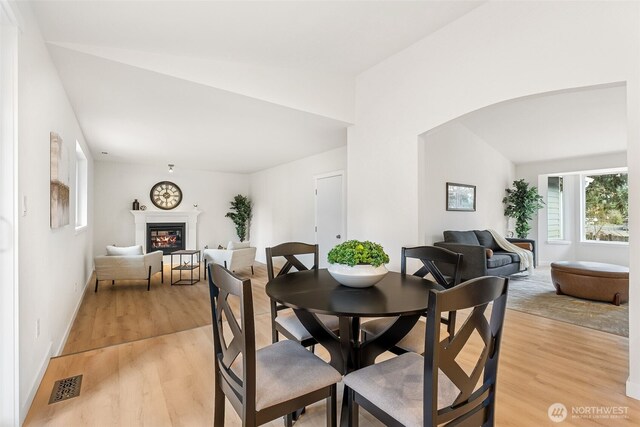 dining area with visible vents, light wood finished floors, lofted ceiling, arched walkways, and a glass covered fireplace