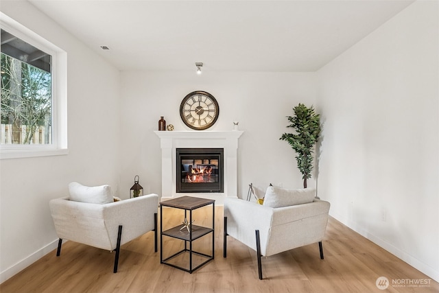 sitting room featuring a glass covered fireplace, light wood-style floors, and baseboards