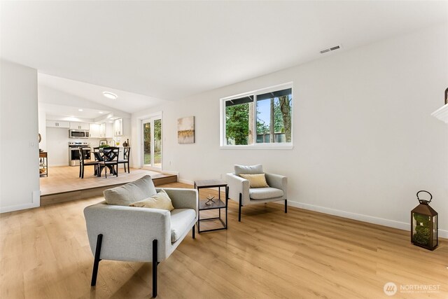 living area with visible vents, baseboards, lofted ceiling, and light wood-style flooring