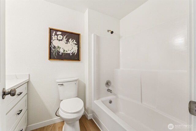 bathroom featuring vanity, wood finished floors, baseboards, shower / washtub combination, and toilet