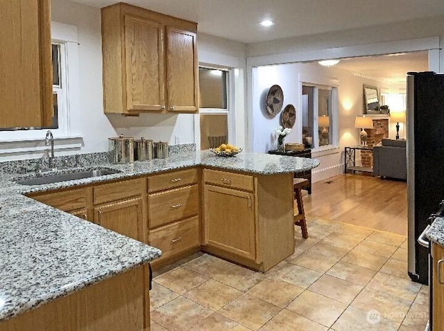 kitchen featuring open floor plan, a peninsula, light stone countertops, and a sink