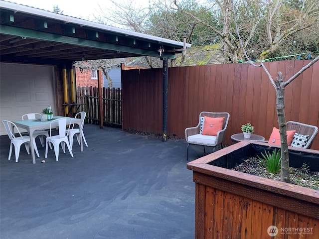 view of patio / terrace with a garage, an attached carport, outdoor dining area, and a fenced backyard