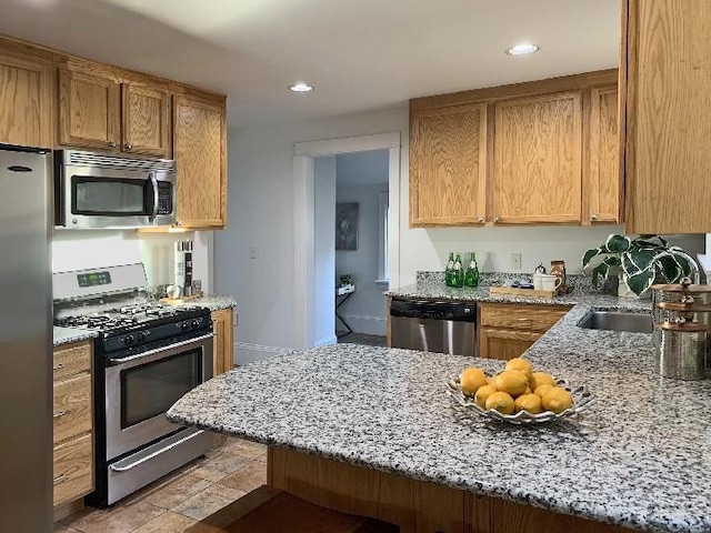 kitchen with light stone countertops, a peninsula, recessed lighting, a sink, and stainless steel appliances