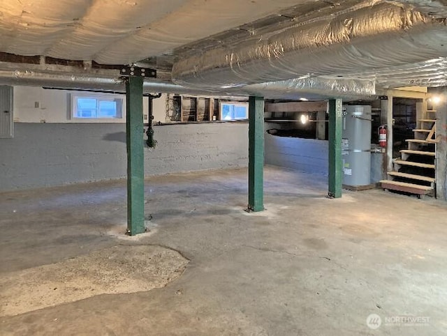 basement featuring strapped water heater, stairway, a healthy amount of sunlight, and electric panel