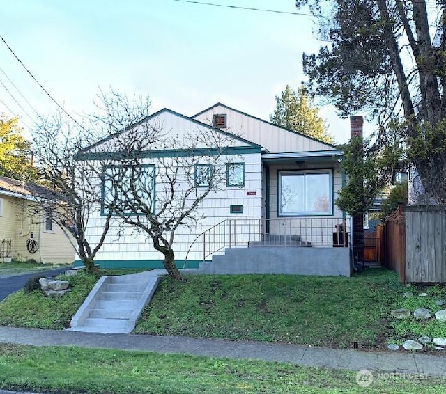 bungalow-style home with metal roof, a chimney, a front lawn, and fence