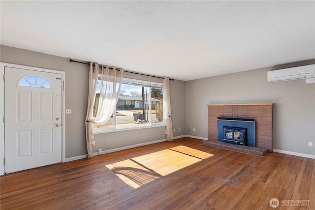 foyer featuring a wood stove, baseboards, an AC wall unit, and wood finished floors