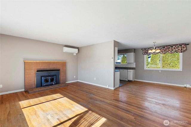 unfurnished living room with baseboards, a chandelier, wood finished floors, and an AC wall unit