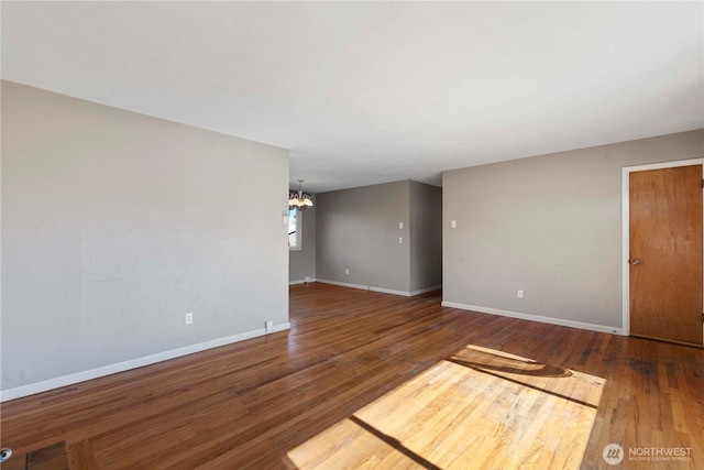 empty room featuring baseboards, wood finished floors, and a notable chandelier