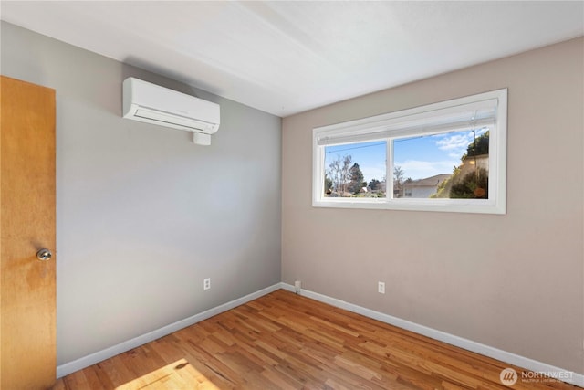 unfurnished room with a wall mounted air conditioner, baseboards, and wood finished floors