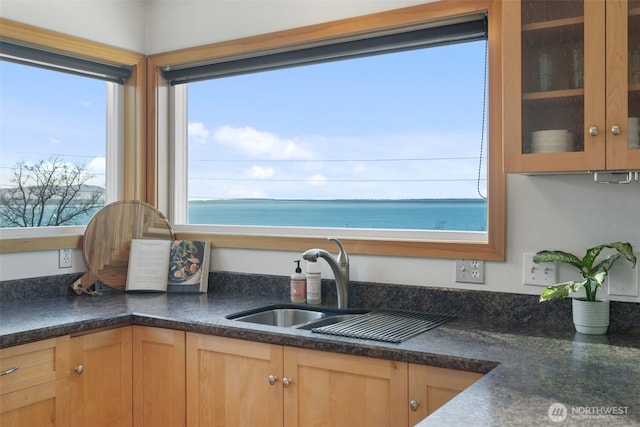 kitchen featuring a water view, light brown cabinets, glass insert cabinets, and a sink