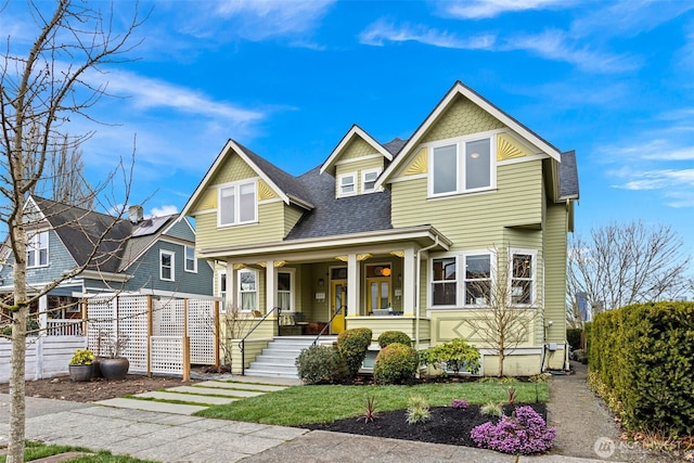 view of front of home with a porch, roof with shingles, and fence