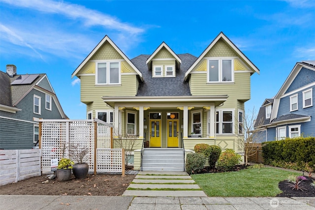 view of front of house with a porch, fence, a front yard, and roof with shingles