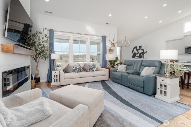 living area with lofted ceiling, visible vents, an inviting chandelier, a glass covered fireplace, and wood finished floors