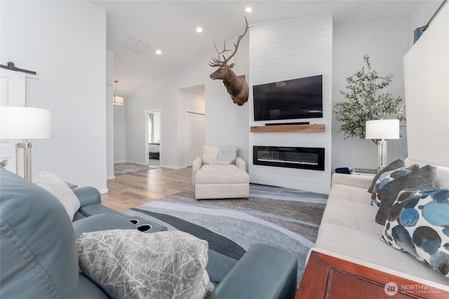 living room featuring recessed lighting, a barn door, a large fireplace, wood finished floors, and high vaulted ceiling