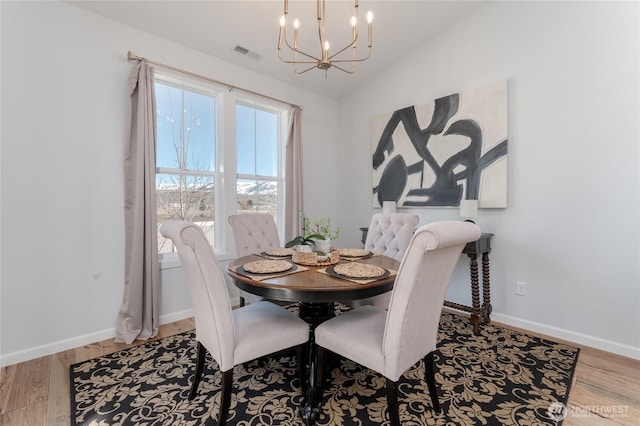 dining room with a chandelier, lofted ceiling, visible vents, and wood finished floors