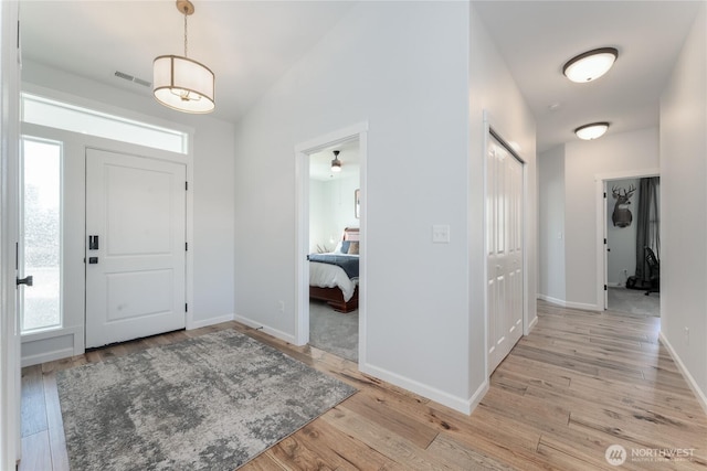 entrance foyer with light wood finished floors, baseboards, visible vents, and vaulted ceiling