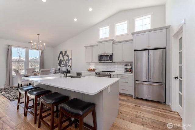 kitchen with stainless steel appliances, a breakfast bar, a sink, light wood finished floors, and an island with sink