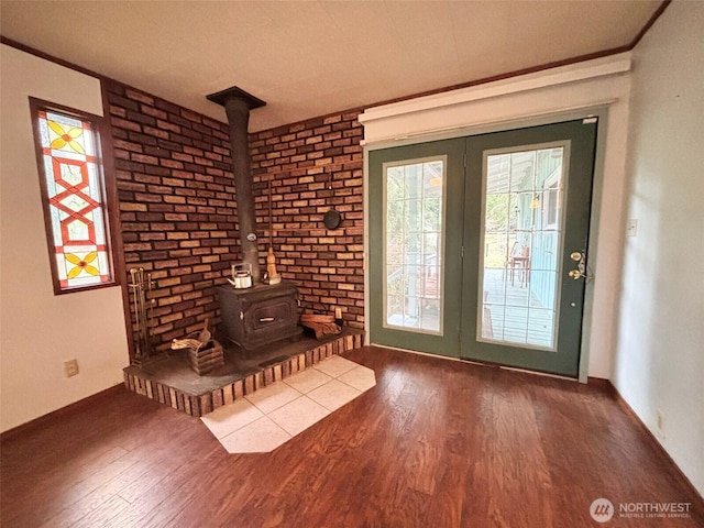 unfurnished living room with baseboards, ornamental molding, wood finished floors, a wood stove, and french doors