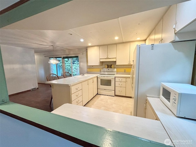 kitchen with white appliances, a peninsula, light countertops, a sink, and recessed lighting