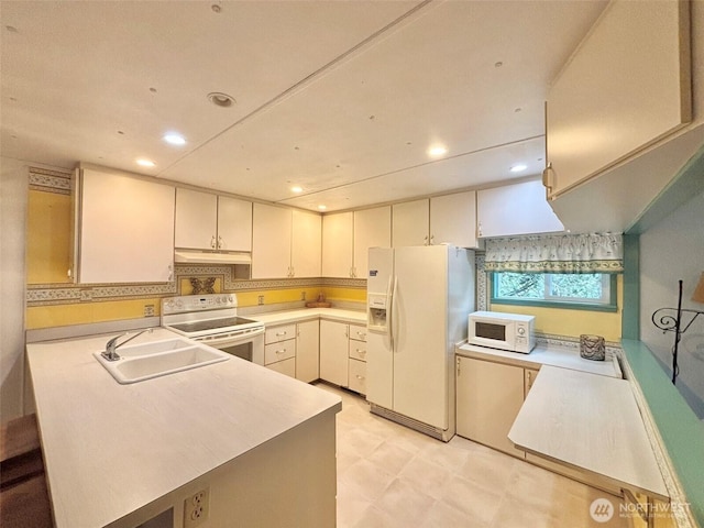 kitchen featuring white appliances, a peninsula, light countertops, under cabinet range hood, and a sink