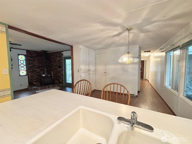 unfurnished dining area with a wood stove, dark wood-style floors, and a ceiling fan