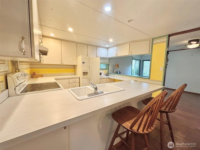 kitchen featuring a peninsula, white appliances, under cabinet range hood, and a sink