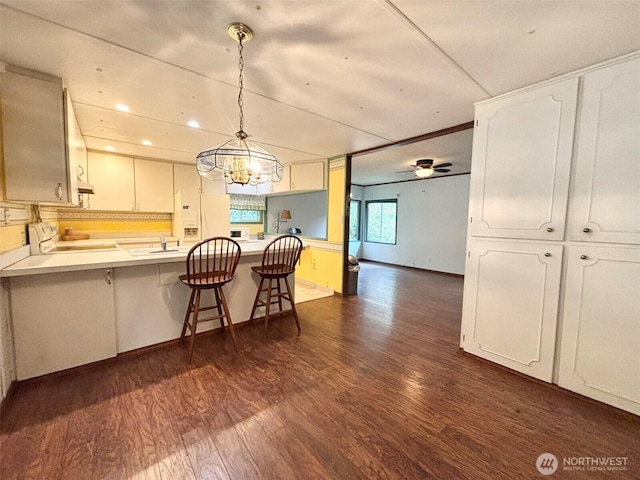 kitchen featuring dark wood-style floors, ceiling fan, stove, a breakfast bar, and a peninsula