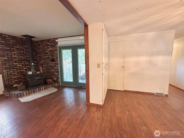 unfurnished living room featuring baseboards, visible vents, wood finished floors, a wood stove, and beam ceiling