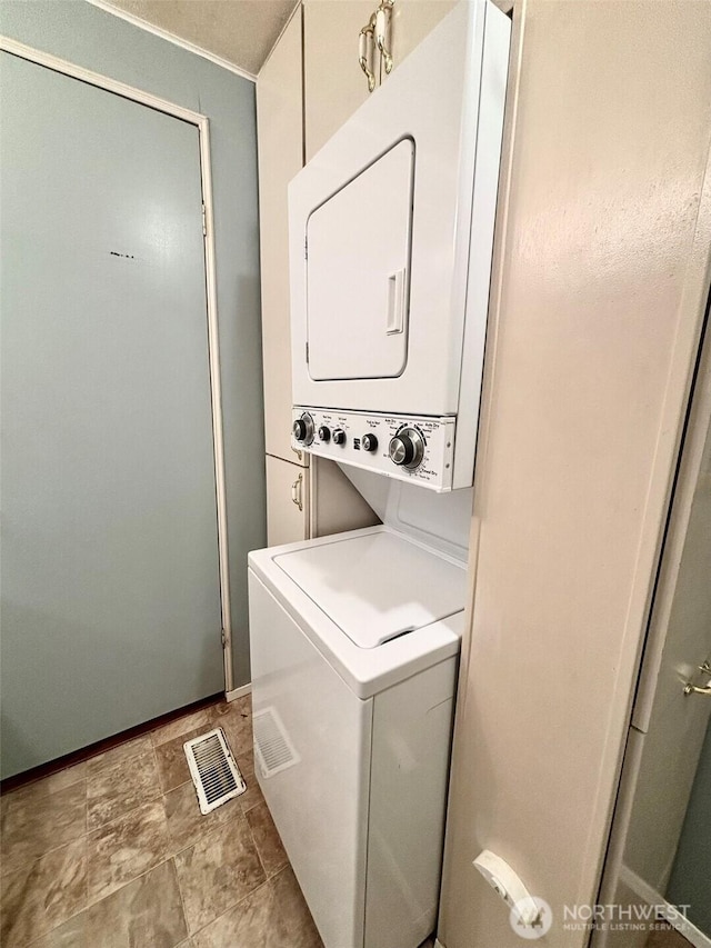 clothes washing area featuring stacked washer and clothes dryer, visible vents, and laundry area